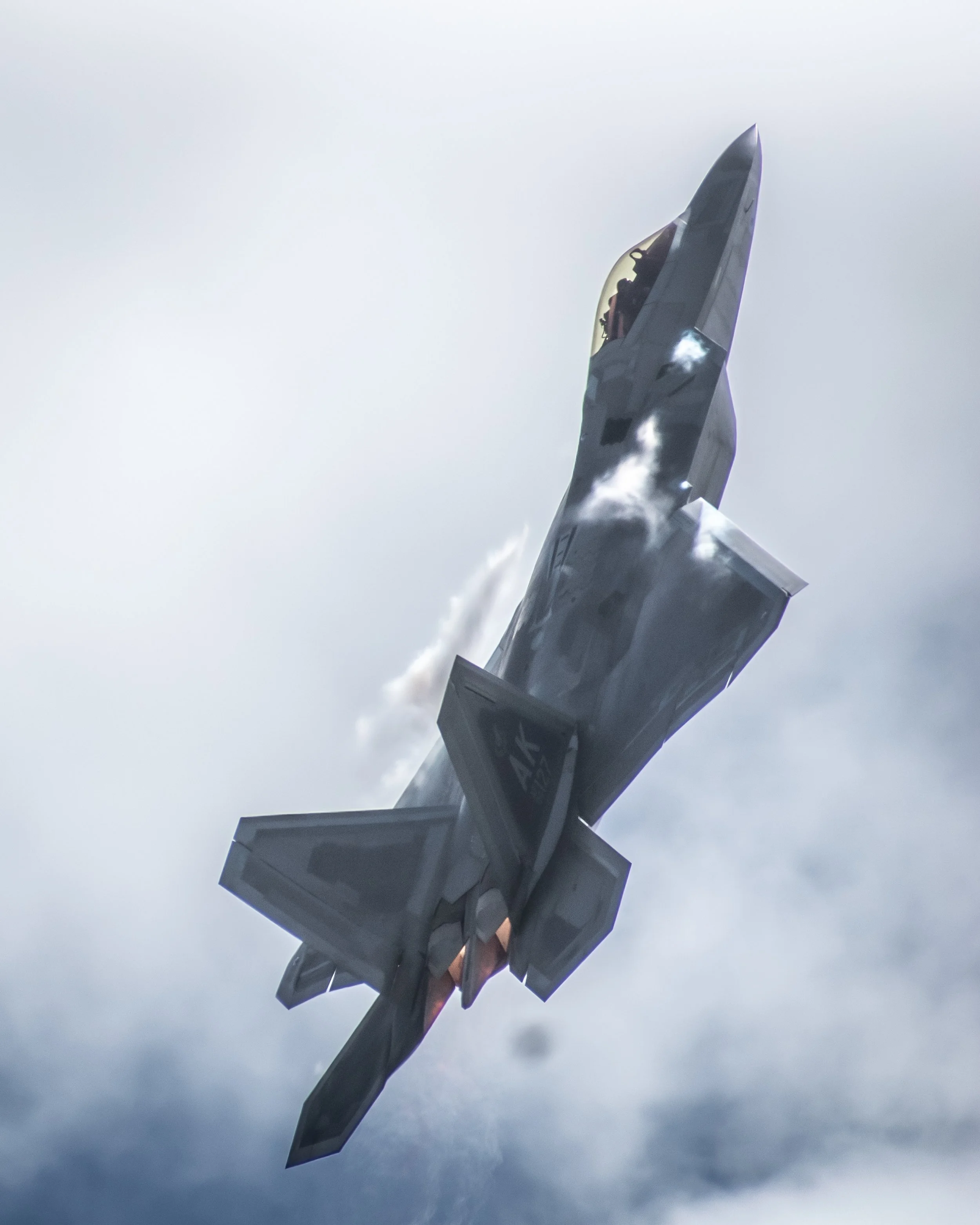 A fighter jet flying at high speed with clouds and sky in the background.