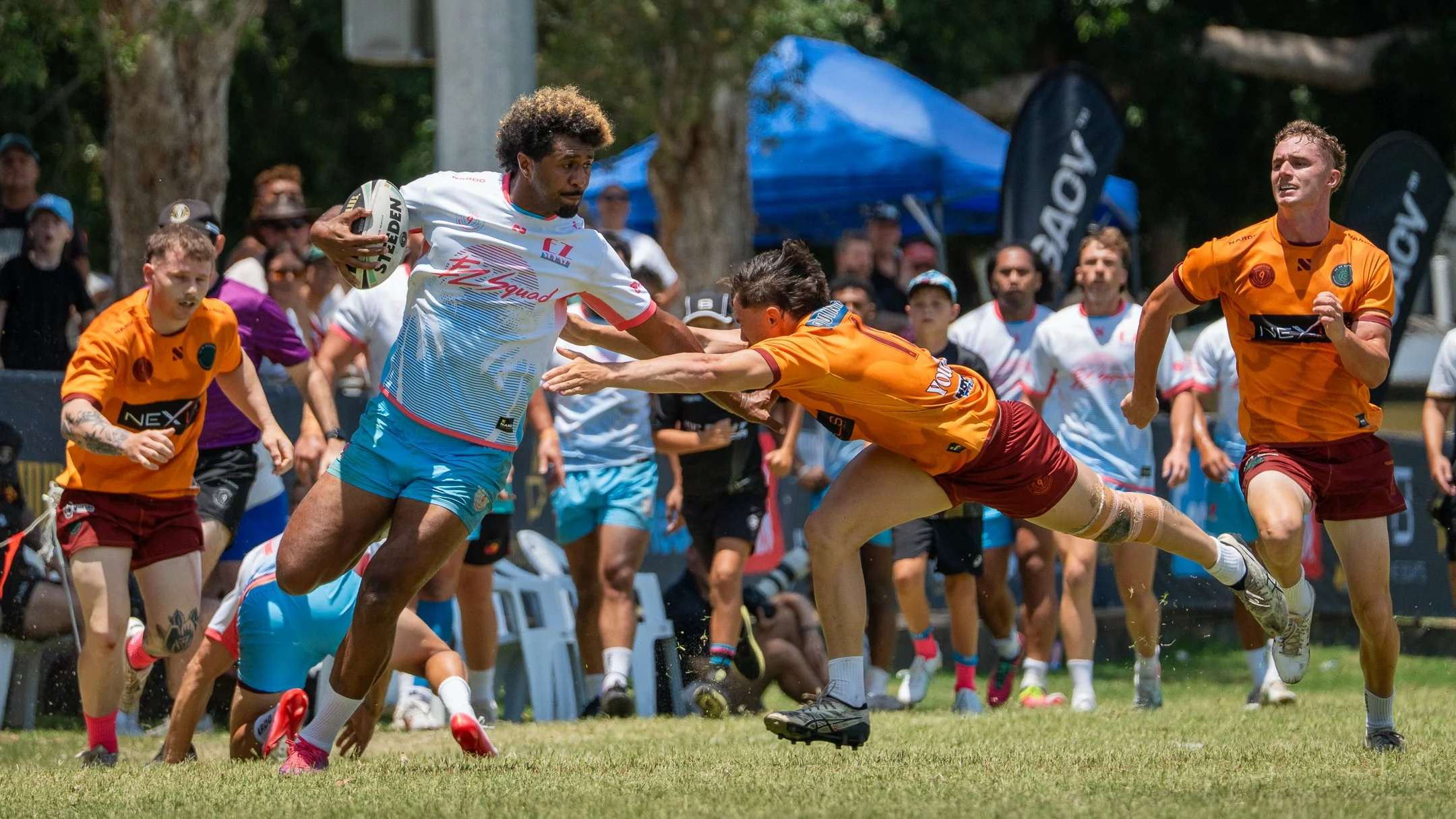 Group of rugby players competing in a match outdoors, with some players running and others tackling.