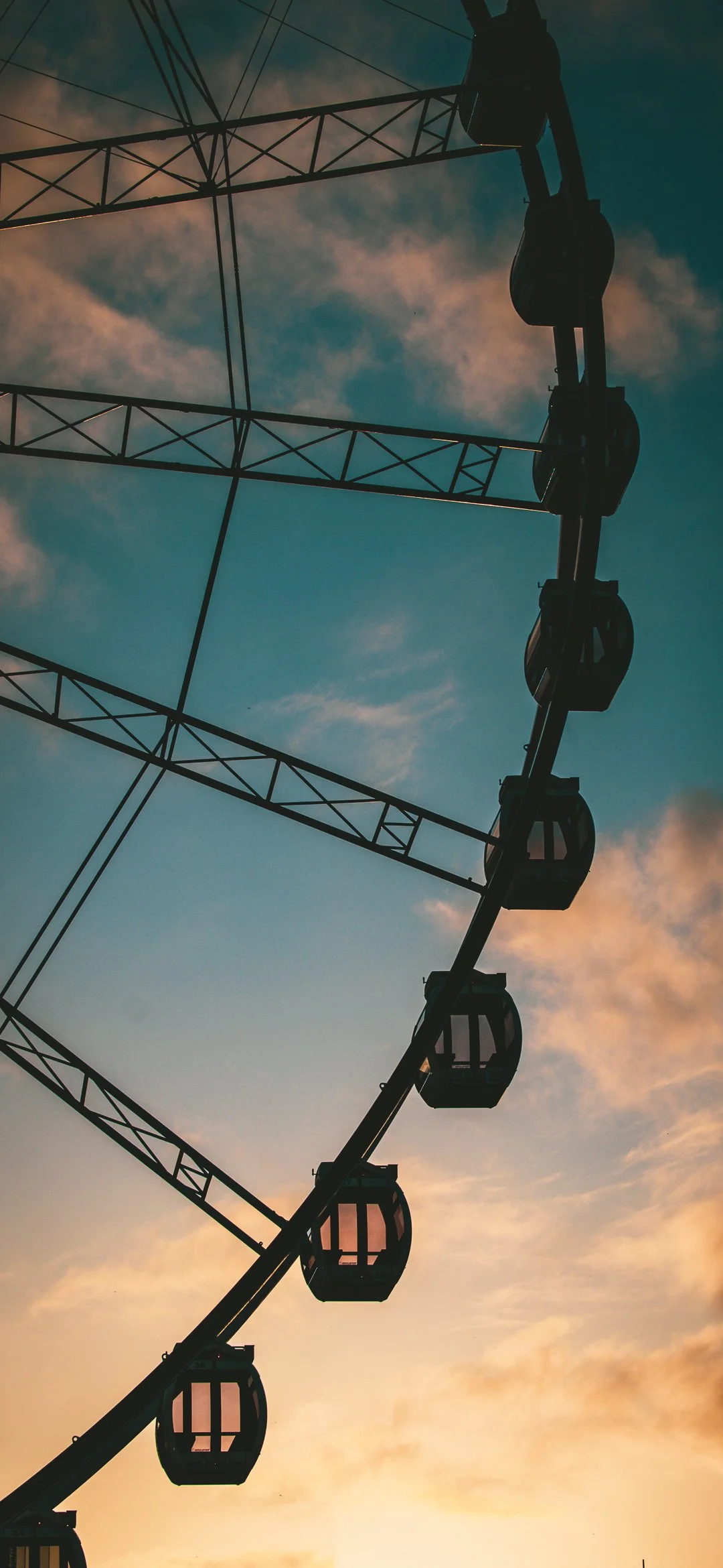 A Ferris wheel silhouette against a sky at sunset with clouds.