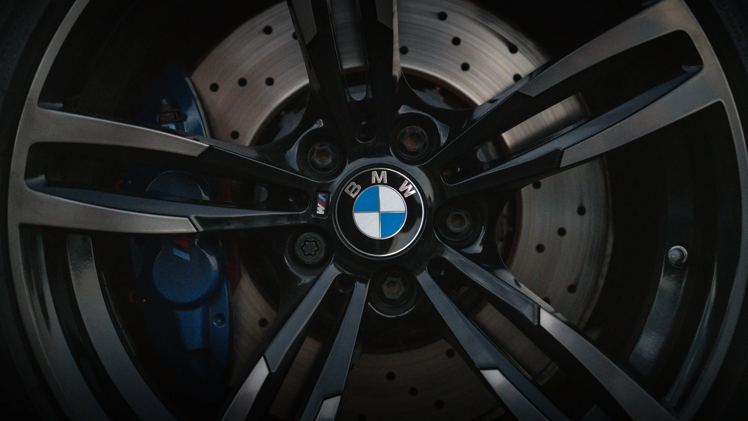 Close-up of a BMW car wheel, showing the black and silver alloy rim with the BMW logo at the center and the brake disc behind it.