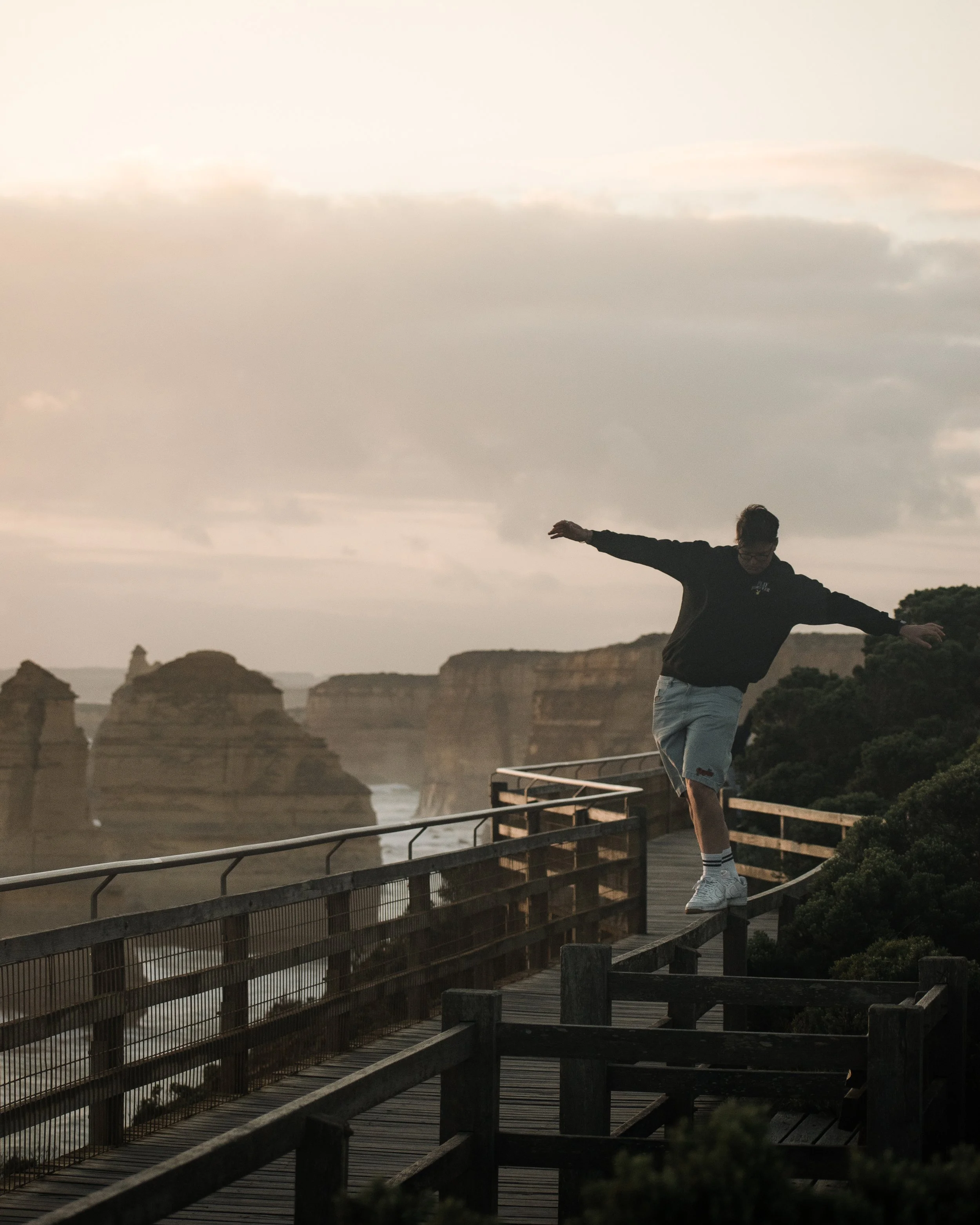 Person running on a wooden boardwalk near a river, with cliffs and cloudy sky in the background, during sunset.