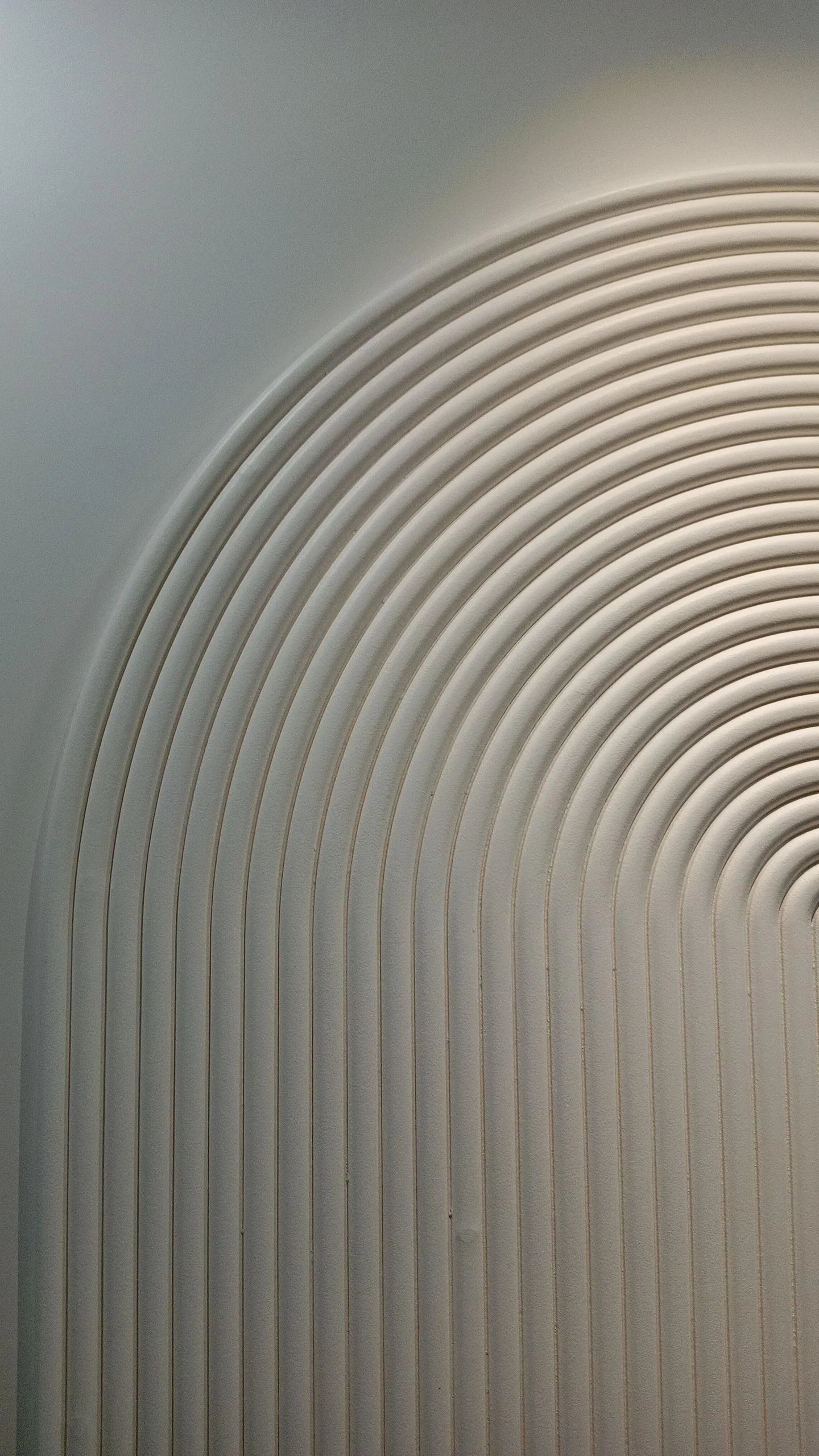 Close-up of a section of a modern wall or ceiling with curved, parallel lines creating a pattern, in neutral tones of gray and beige.