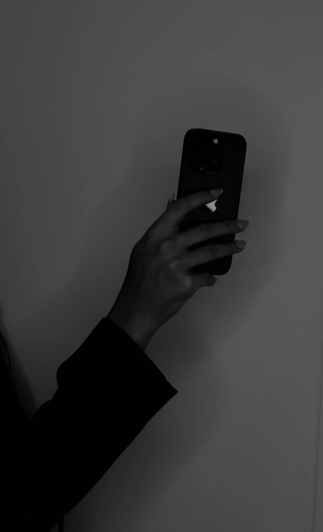 Black and white photo of a person's hand holding a smartphone against a plain wall background.