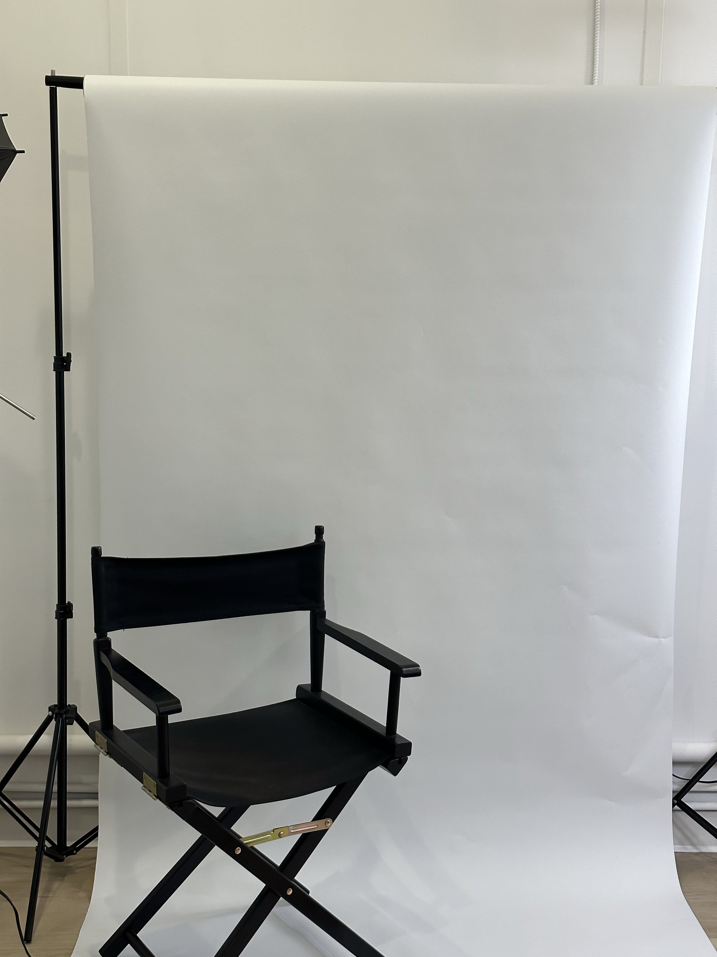 A director's chair on a black stand in front of a white background, with studio lighting equipment visible on the left.