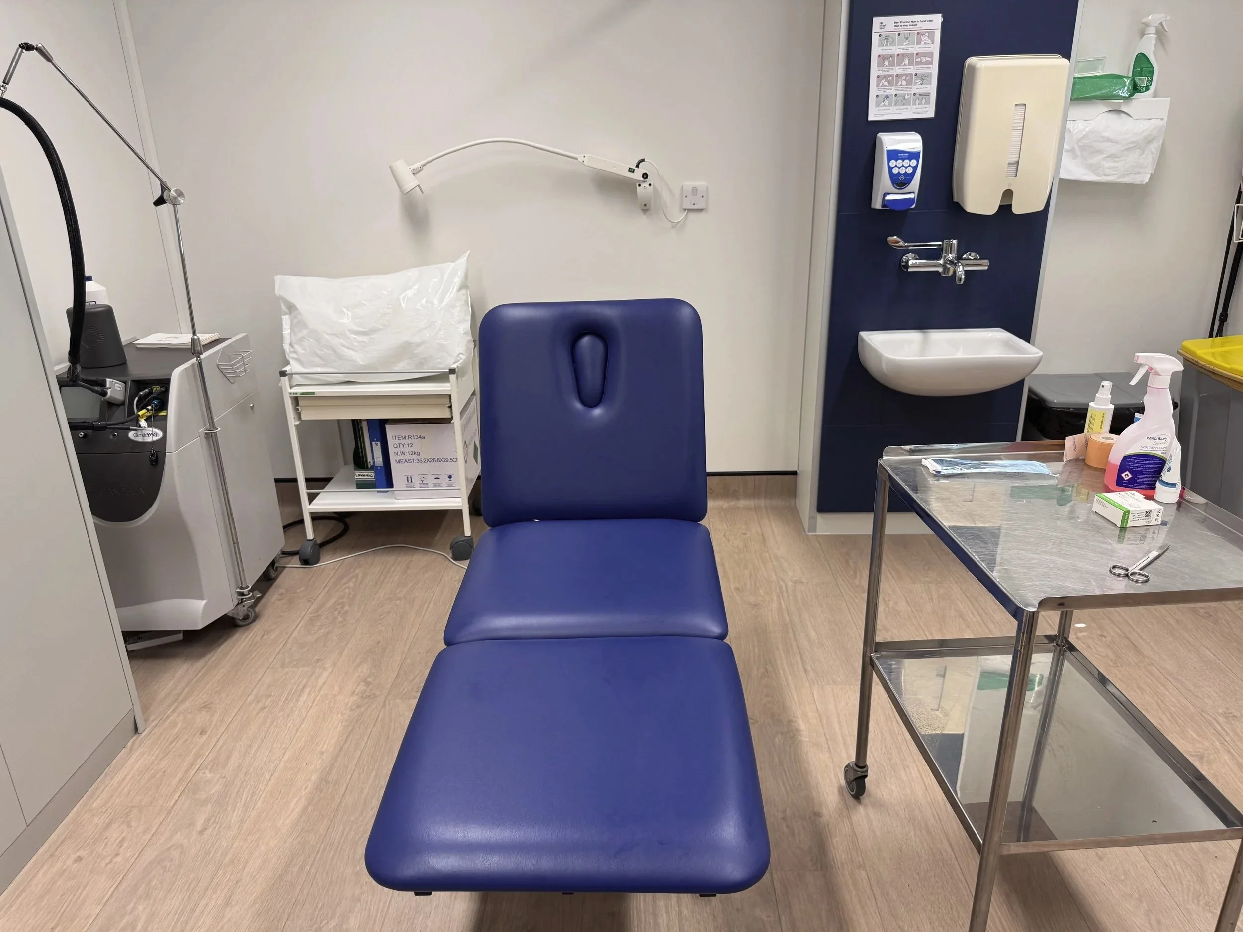 Empty hospital room with a blue chair, medical equipment, and supplies on a metal cart.
