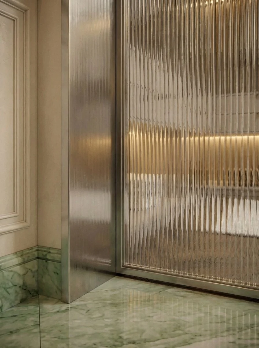 Close-up of a corner with metallic sliding door, textured glass panel, marble flooring, and a cream-colored wall with decorative molding.