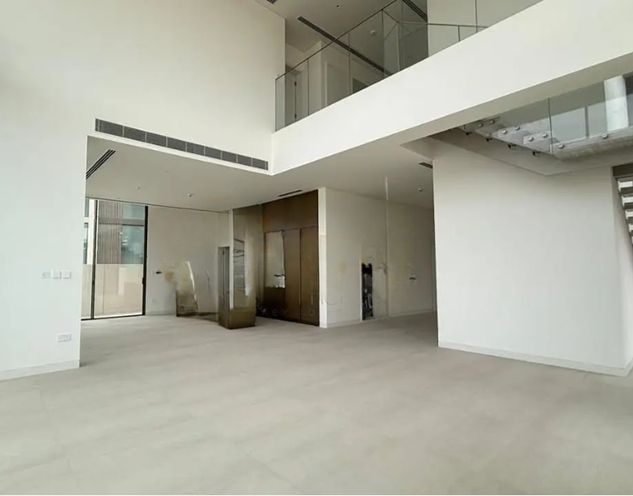 Empty modern interior space with white walls, light-colored flooring, and an open layout, featuring a staircase and balcony.
