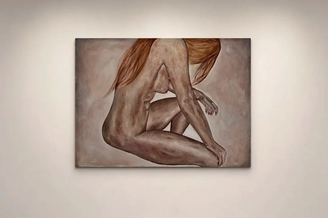 Painting of a nude woman with long hair, sitting with her legs pulled close to her chest and her arms wrapped around her knees, in an art gallery.