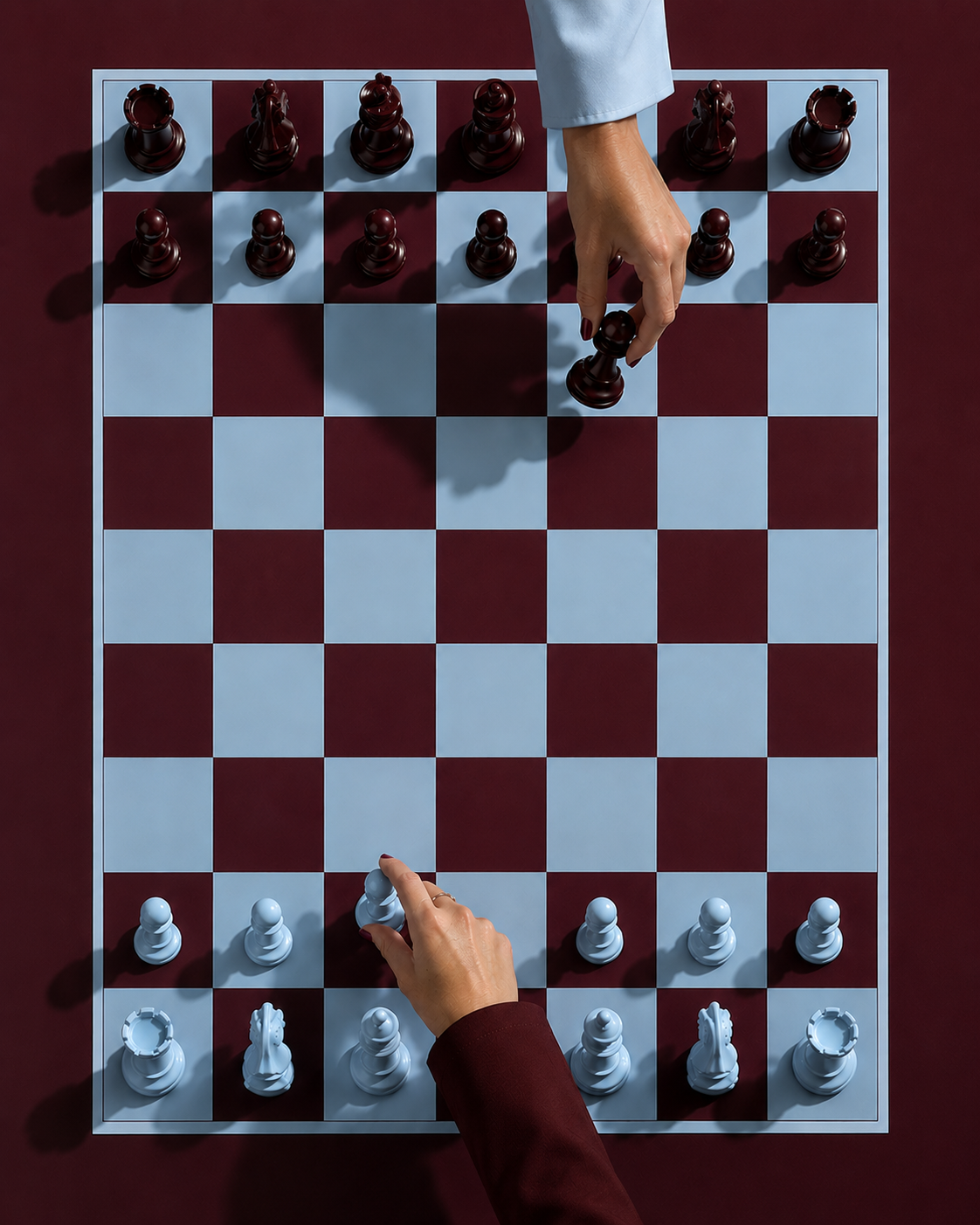 A chess game in progress with blue and burgundy pieces on a chessboard, viewed from above, with two people making moves.