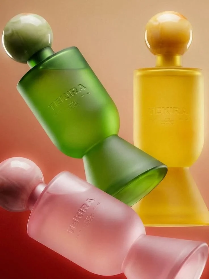 Three colorful glass perfume bottles, one green, one yellow, and one pink, with spherical caps, arranged on a pink surface.