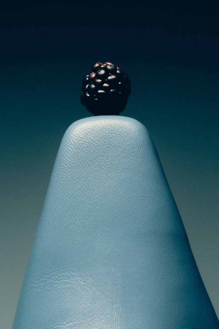 A blackberry balancing on the rounded tip of a blue, textured cone-shaped object.