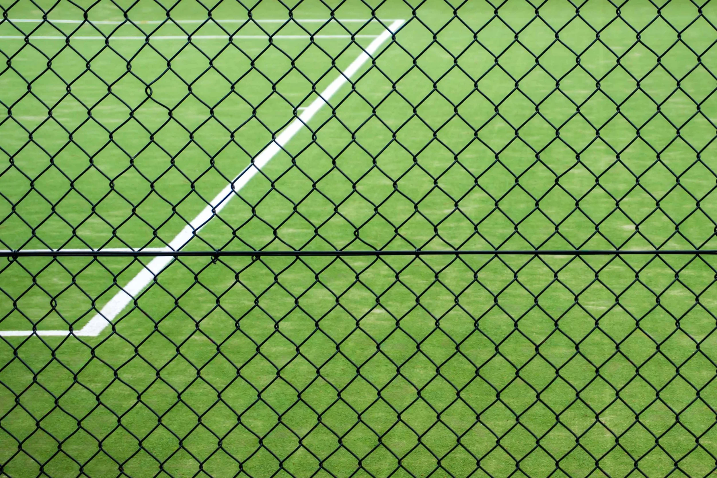 Tennis court with green surface and white lines seen through black chain-link fence — abstract fine art photography by Kimberly Poppe, ZOZI Gallery Sitges