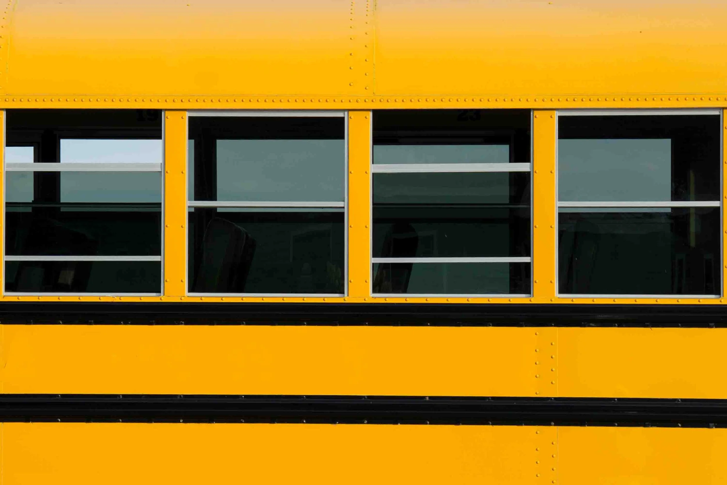 Close-up of yellow school bus windows and rivets — graphic color-field composition by Kimberly Poppe, American fine art photographer based in Spain.
