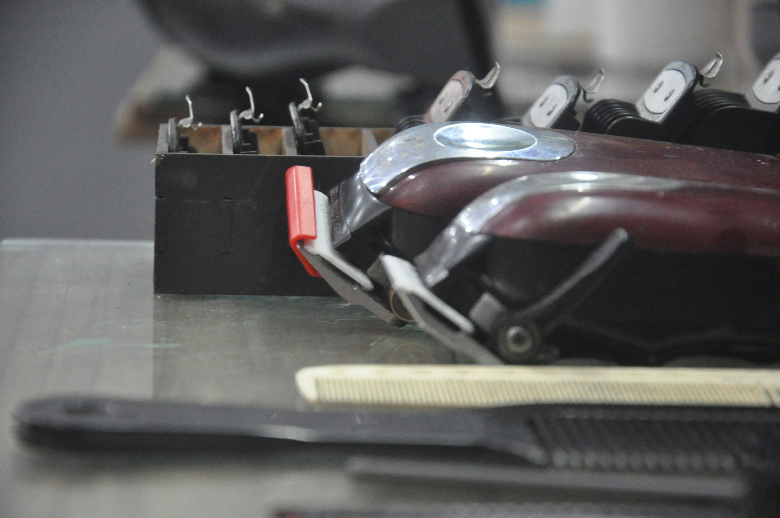 Close-up view of a metal object with hooks and a red handle, possibly part of a mechanical or industrial equipment, on a gray surface.