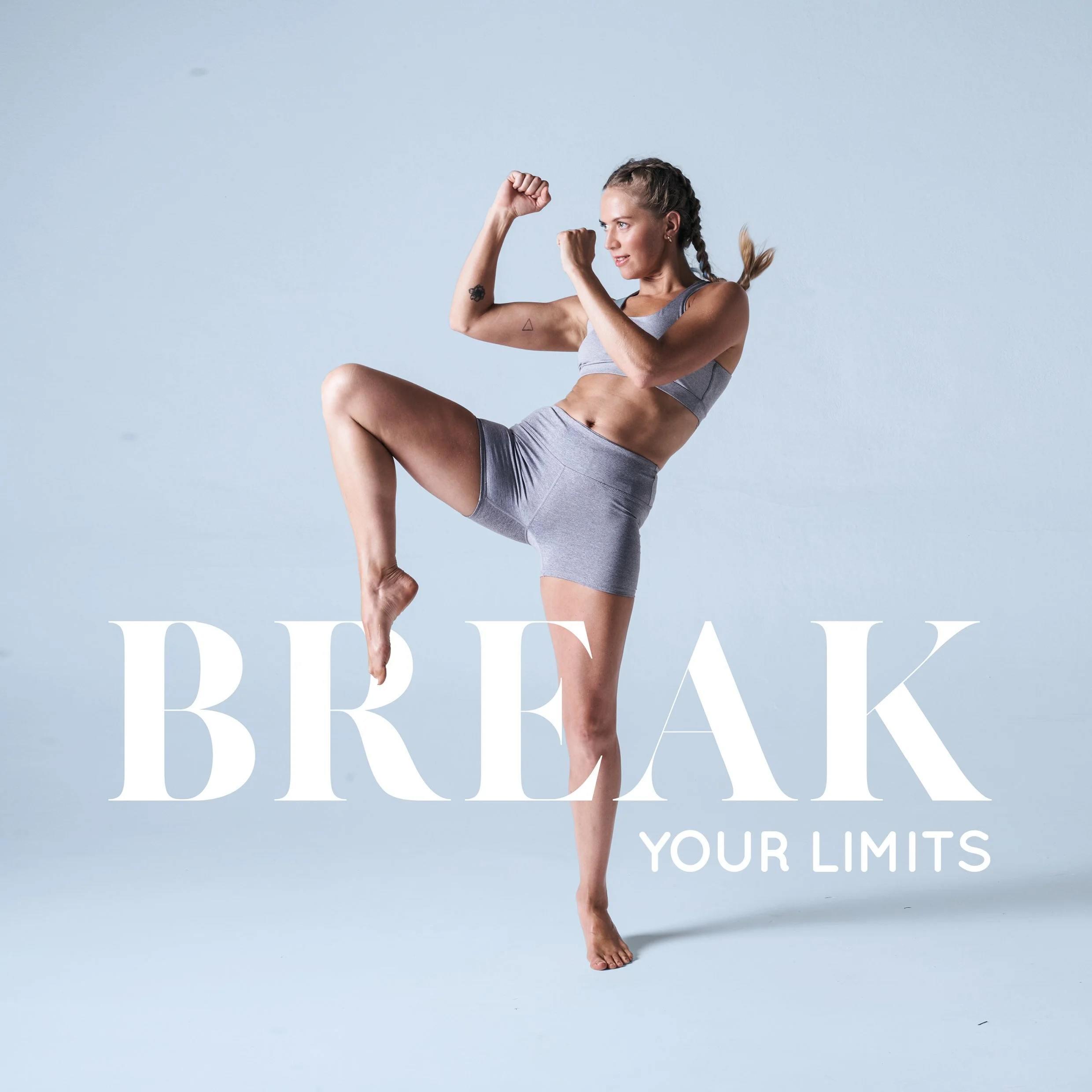 A woman wearing gray athletic clothing flexing her biceps and standing on one leg with the other knee raised, against a light blue background with white text that says "BE YOUR LIMITS."