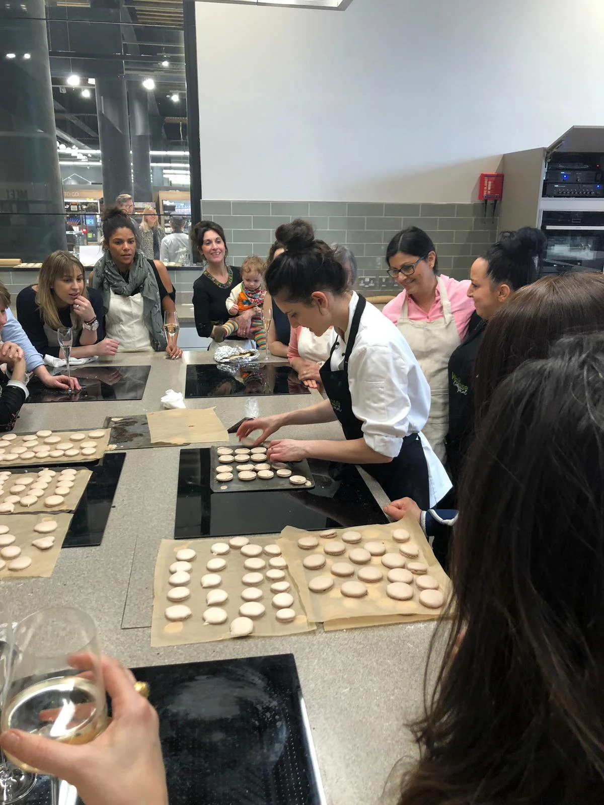 People in a cooking class making macarons in a kitchen with baking trays and parchment paper.