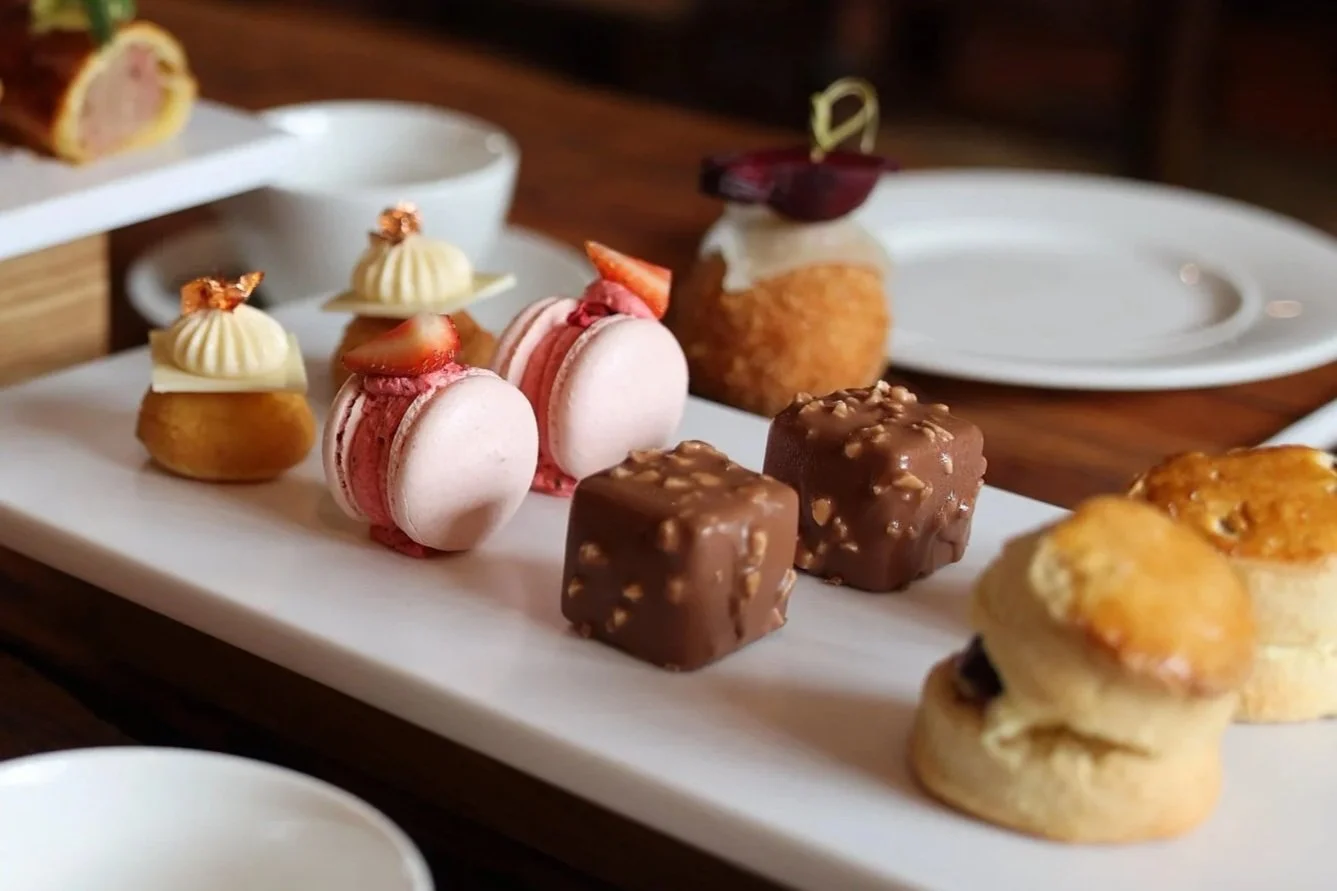 Assorted small desserts on a white rectangular platter, including macarons, chocolates, and cream-filled pastries.