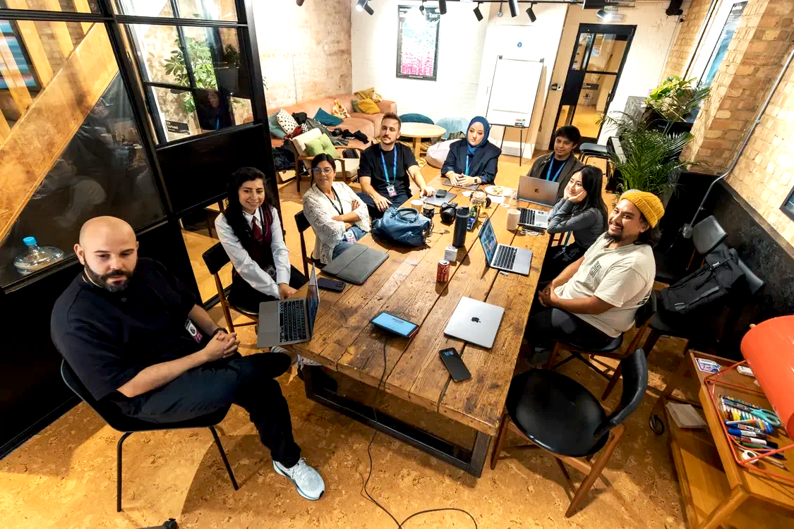 Menschen bei einer Besprechung in einem modern eingerichteten Raum mit Holzdecke und großen Fenstern, mit Laptops, Kaffeetassen und Notizbüchern auf dem Tisch.