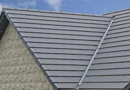 Close-up of a gray metal roof with a textured beige wall and blue sky background.