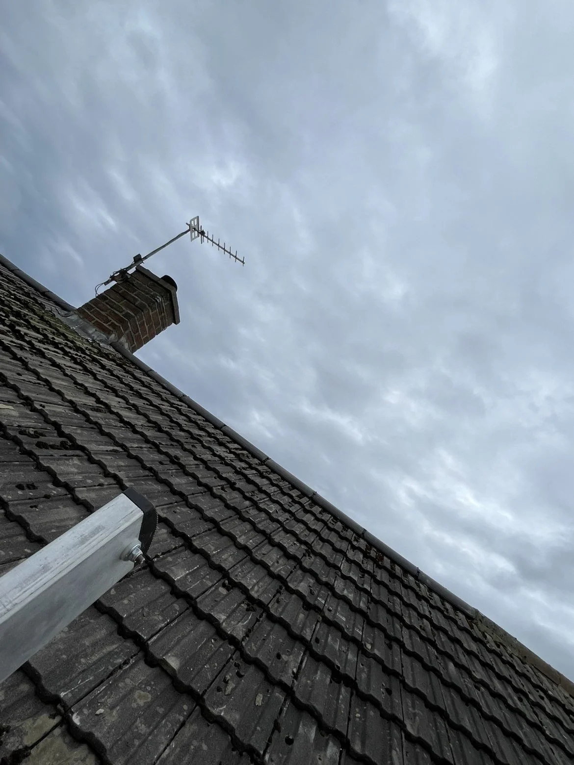 View of a brick chimney with an antenna on the roof under a cloudy sky.