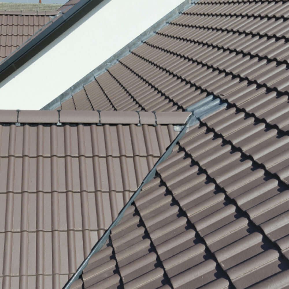 Close-up view of brown metal roofing tiles on a sloped roof with a ridge cap and a seam between two sections.