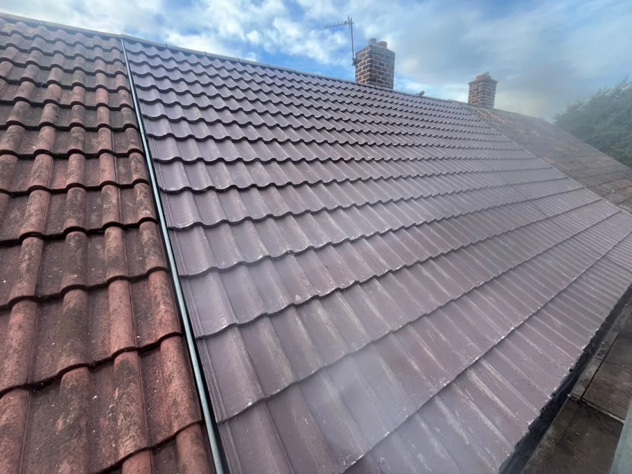 Comparison of two sections of a house roof: one with old weathered tiles and the other with newly installed clean tiles, separated by a metal flashing.
