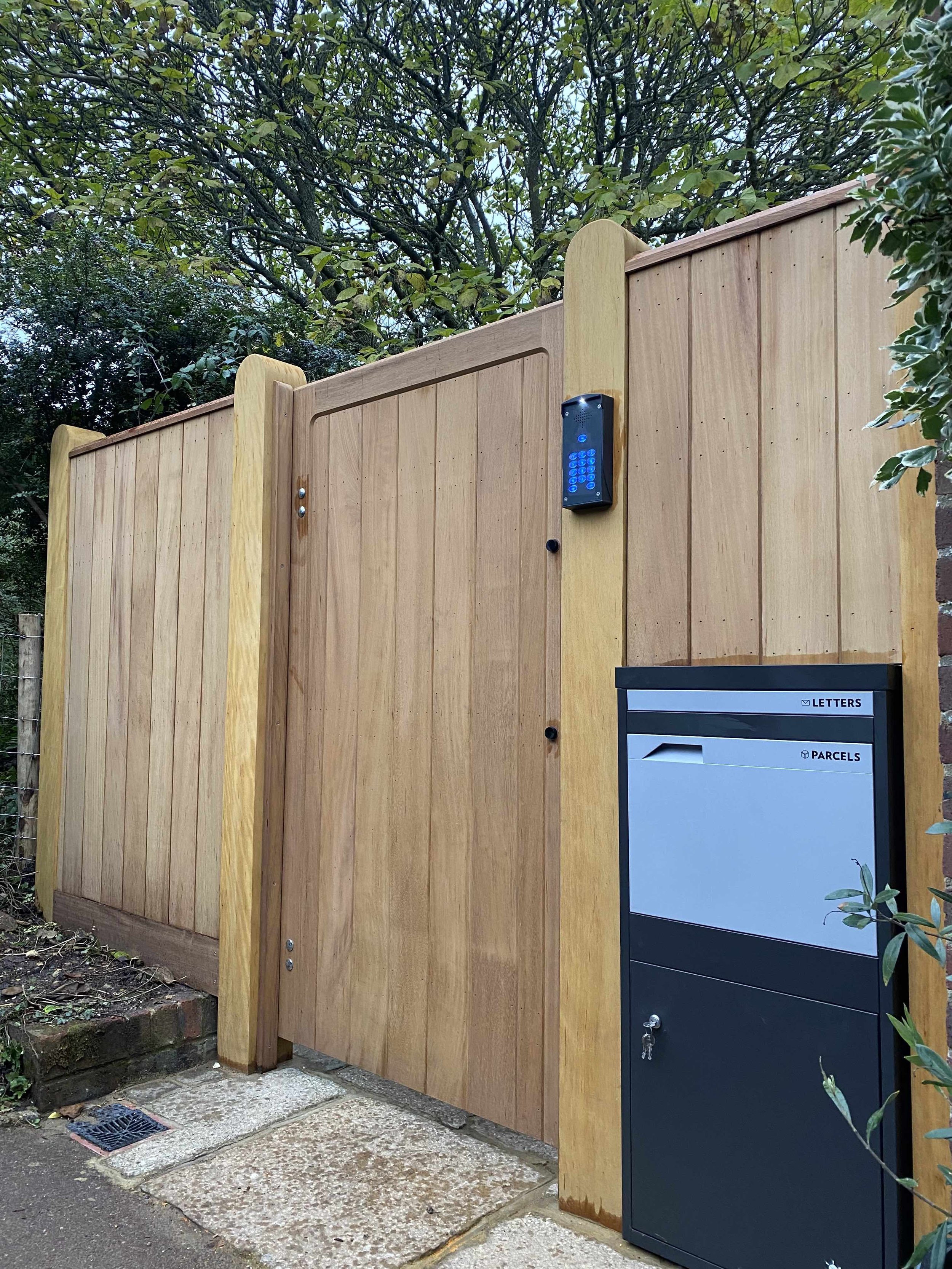 A wooden fence with a black parcel and letter box attached, situated near a tree and some bushes.