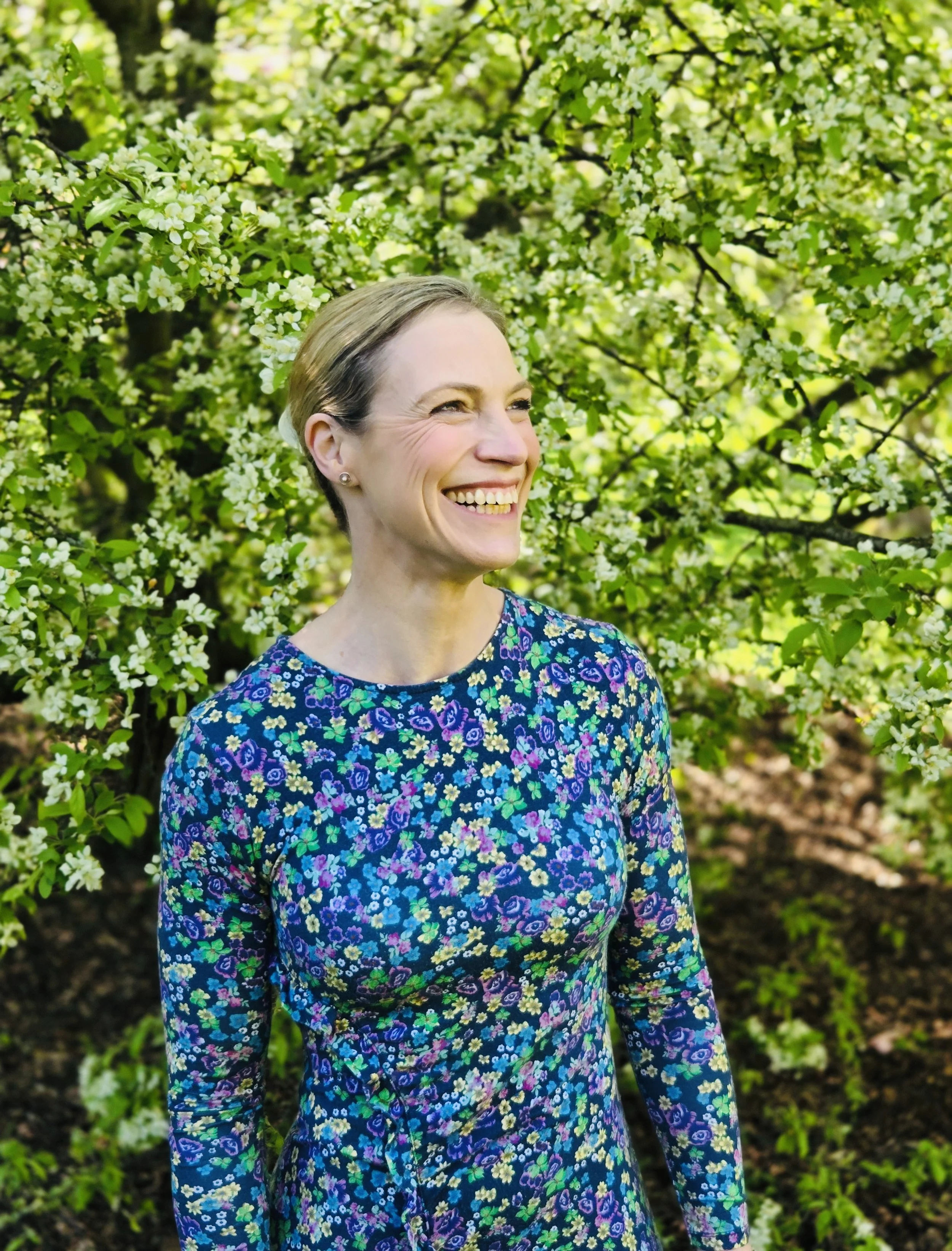 Lesley Buchan, soprano and vocal coach, smiling in a dress in front of a floral background