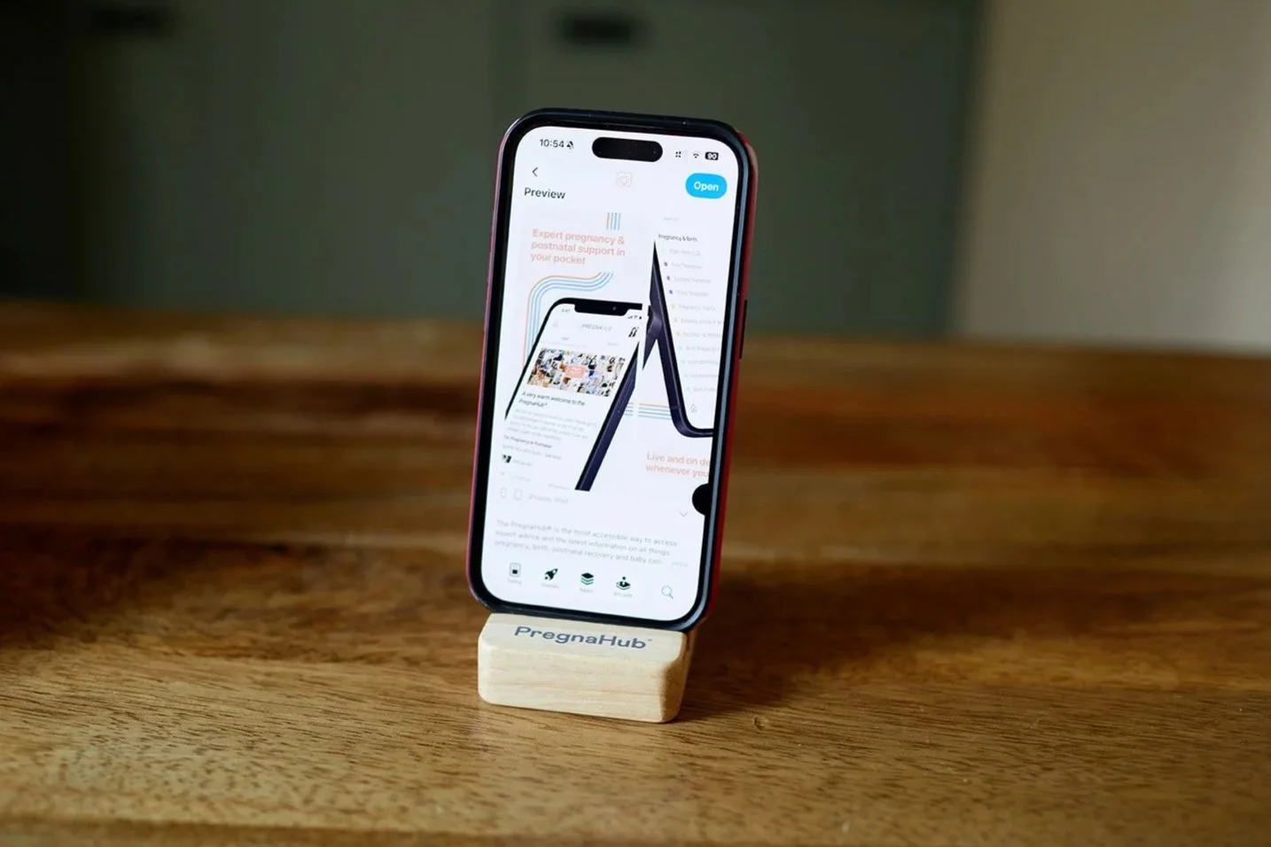 Smartphone displaying a webpage, standing on a wooden block labeled 'PregnaHub', on a wooden table.