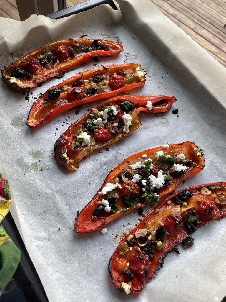 Roasted red peppers stuffed with cheese, cherry tomatoes, black and green olives, and herbs, placed on baking sheet with parchment paper.