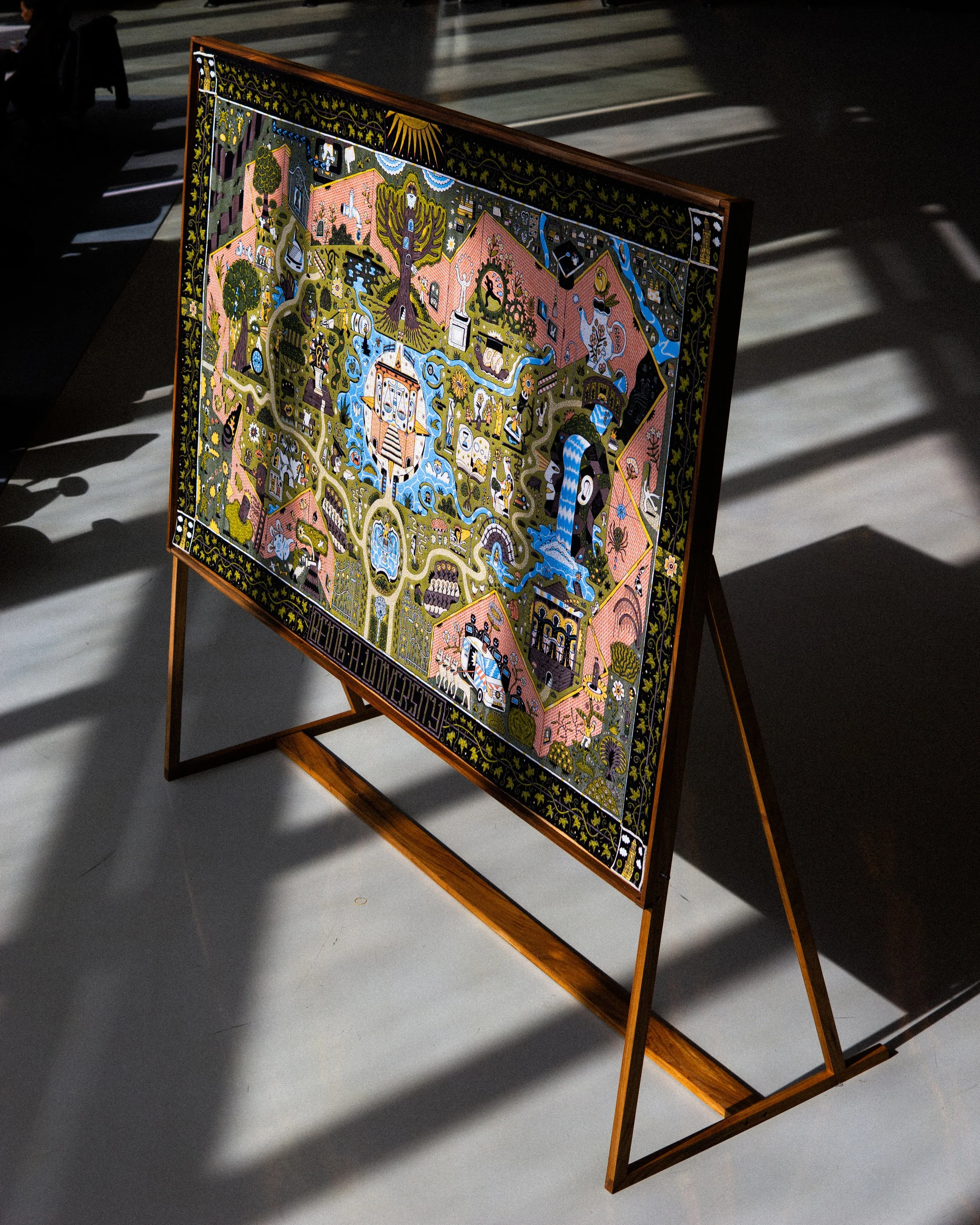 A colorful, detailed artwork or tapestry on an easel, featuring various scenes with people, animals, and nature elements, set in a gallery with shadows cast on the floor.  Tapestry and jacquard weaving art