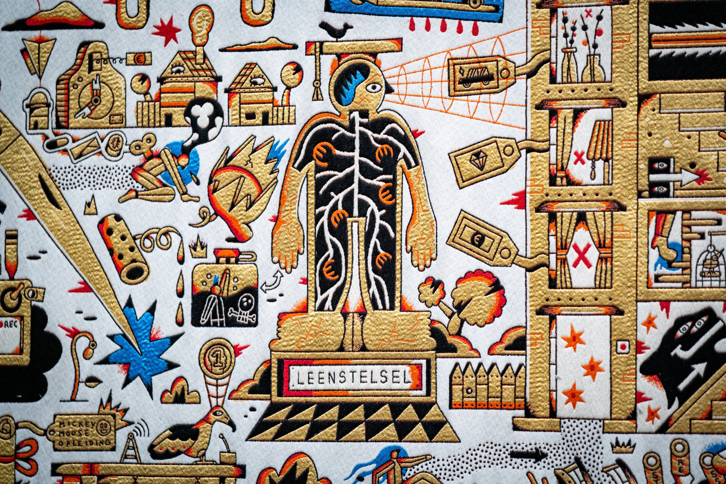 A detailed embroidered patch depicting a stylized human anatomy with electrical and mechanical elements, surrounded by various technical symbols, tools, and objects, including a laptop, a spray bottle, and geometric shapes, in a primarily gold, black
