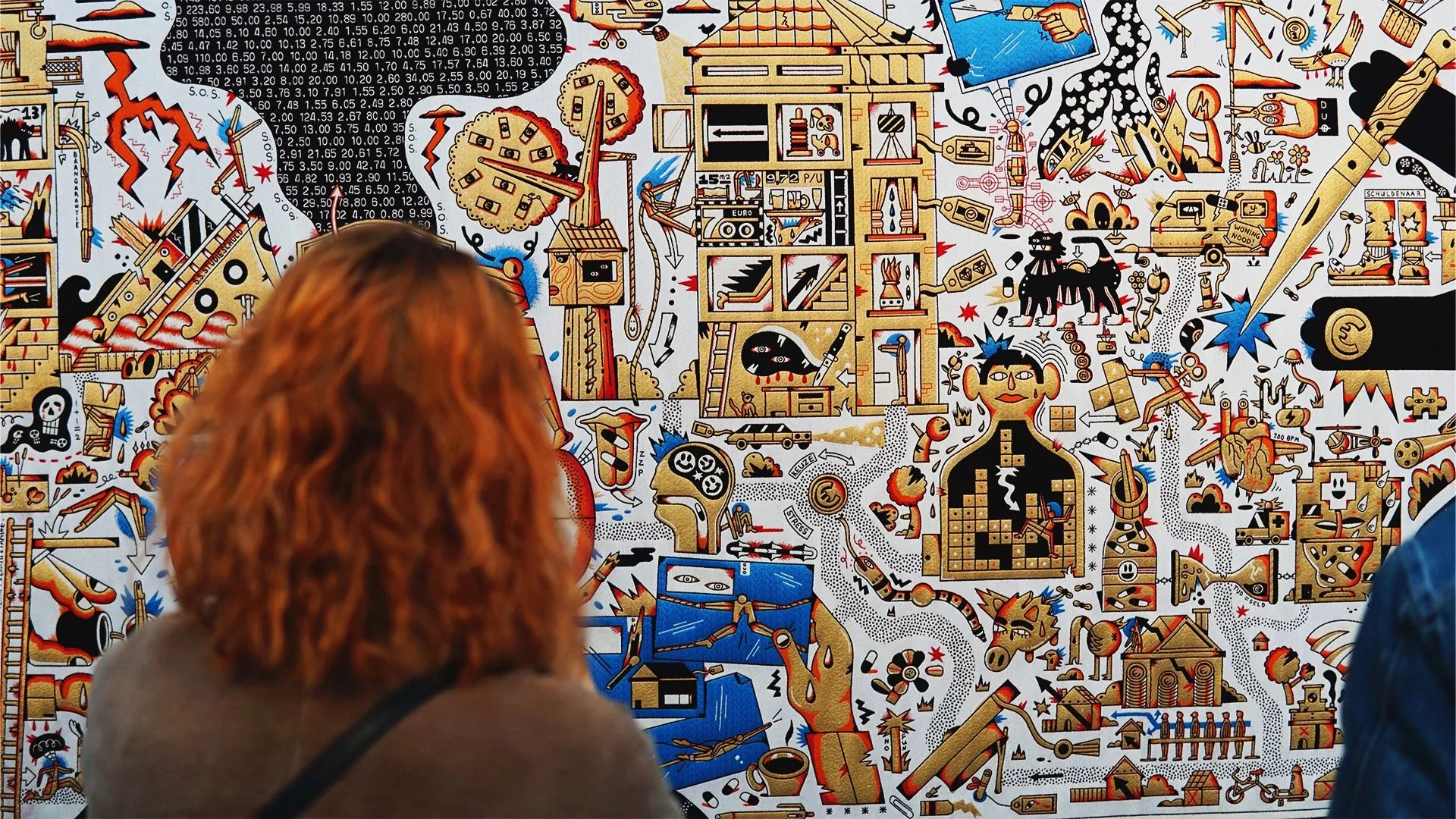 People observing a colorful, detailed, abstract artwork or mural with various symbols, figures, and imagery.  Tapestry and jacquard weaving art