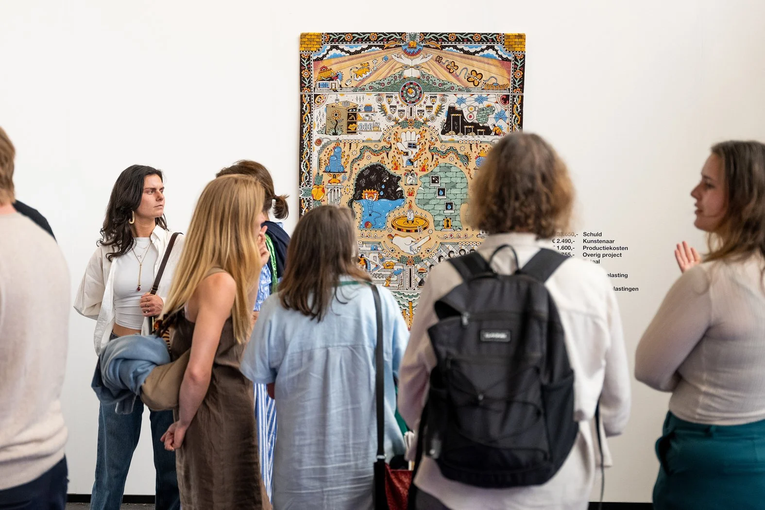 Group of people viewing a colorful artwork in a gallery, with some discussing and others observing.