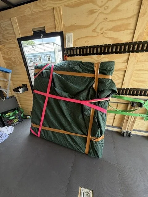 Heavy six-foot by six-foot oil painting blanket-wrapped and secured with multiple straps inside Slohaven Transfer's enclosed trailer.