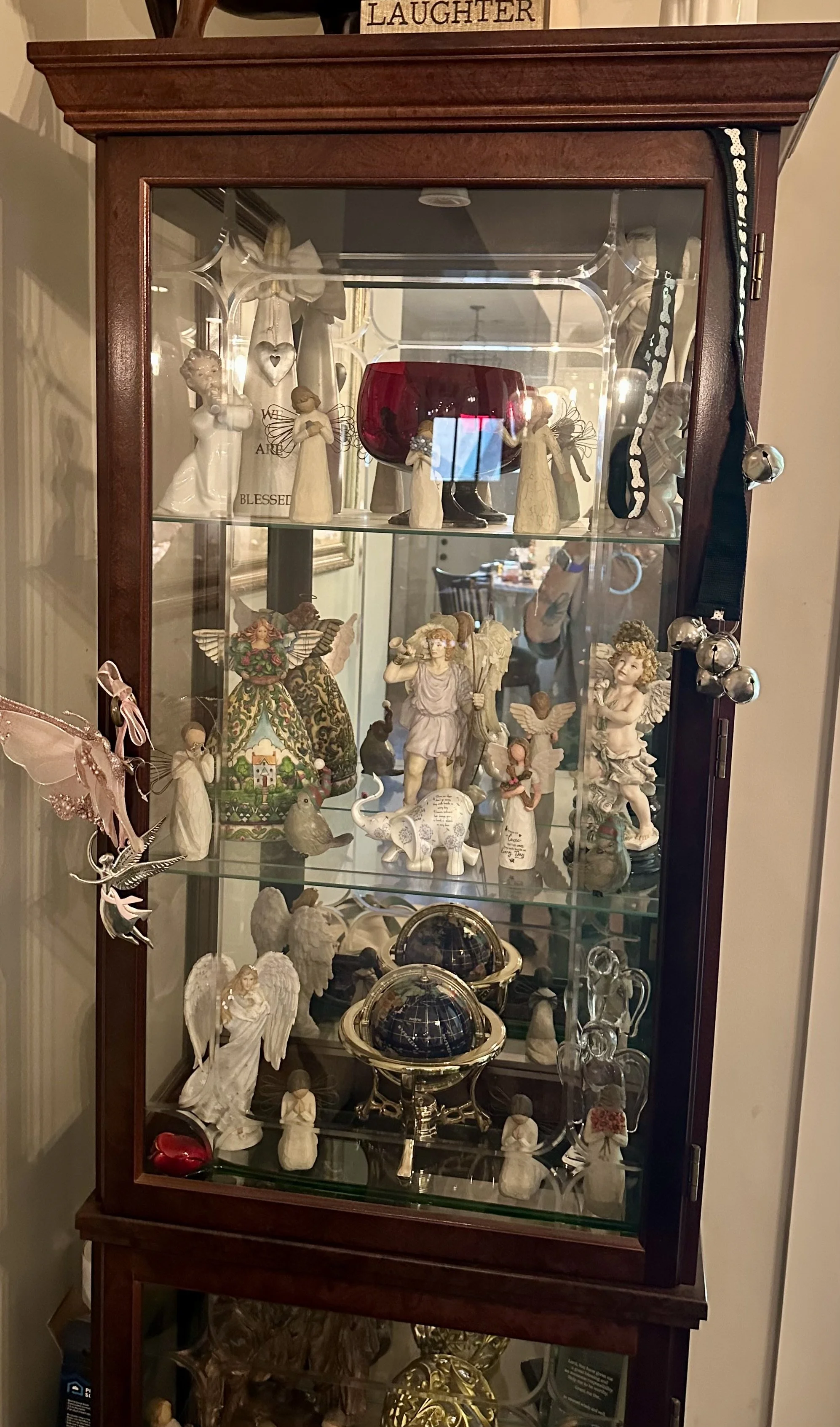 A wooden display cabinet with glass shelves holding decorative figurines of angels, animals, and other artistic pieces, along with a red glass bowl on the top shelf delivered to Washington DC.