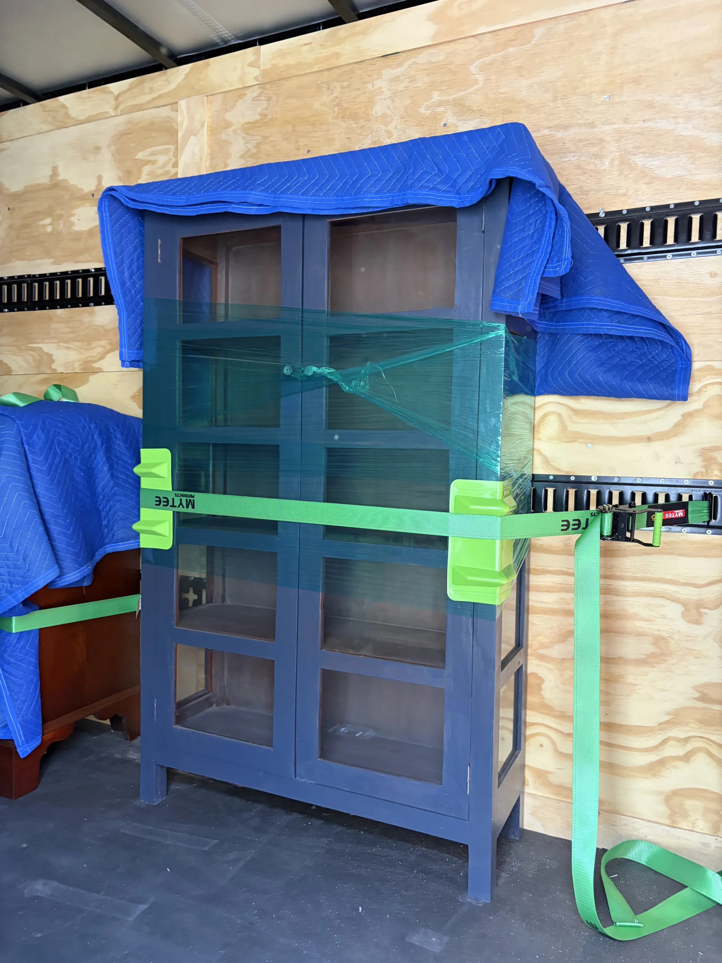 Antique cabinet protected with moving blankets, stretch wrap, corner guards, and E-track securement inside Slohaven's enclosed trailer.