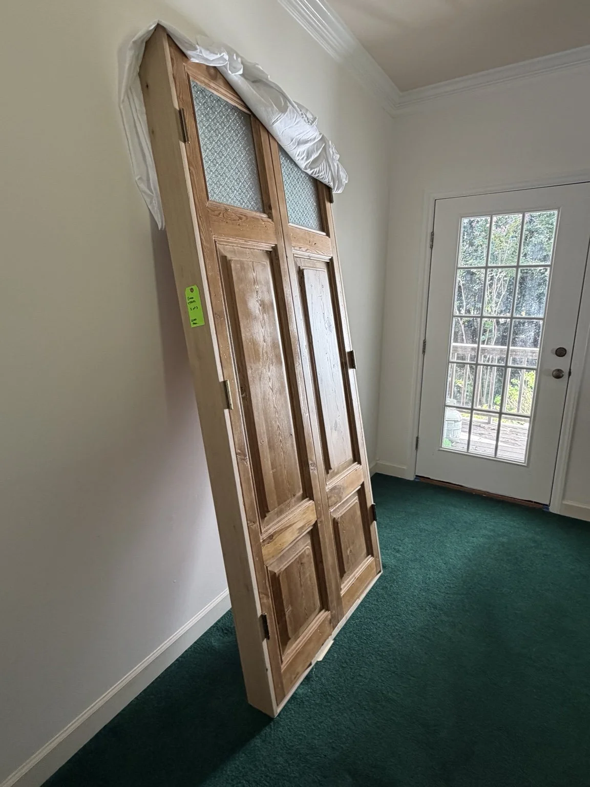Tall wooden architectural doors with textured glass panels standing indoors after delivery, with padding protecting the upper edge.