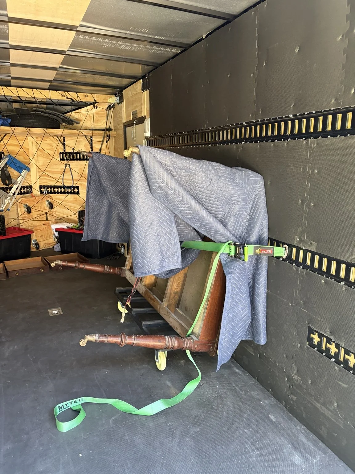 Early-1900s library table protected with moving blankets and a green E-track strap inside Slohaven Transfer’s enclosed trailer.