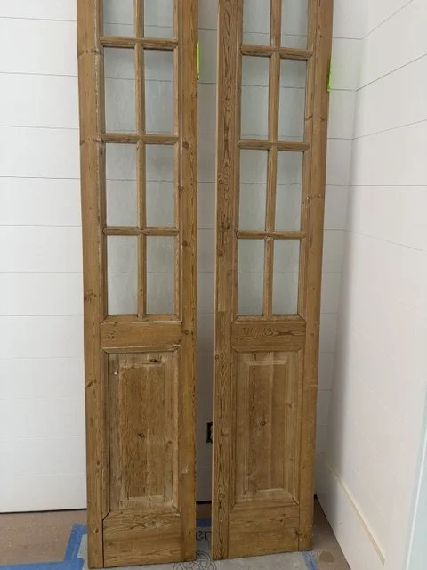 Two tall wooden glass-paneled door sections leaning against a white interior wall after delivery in Florida.