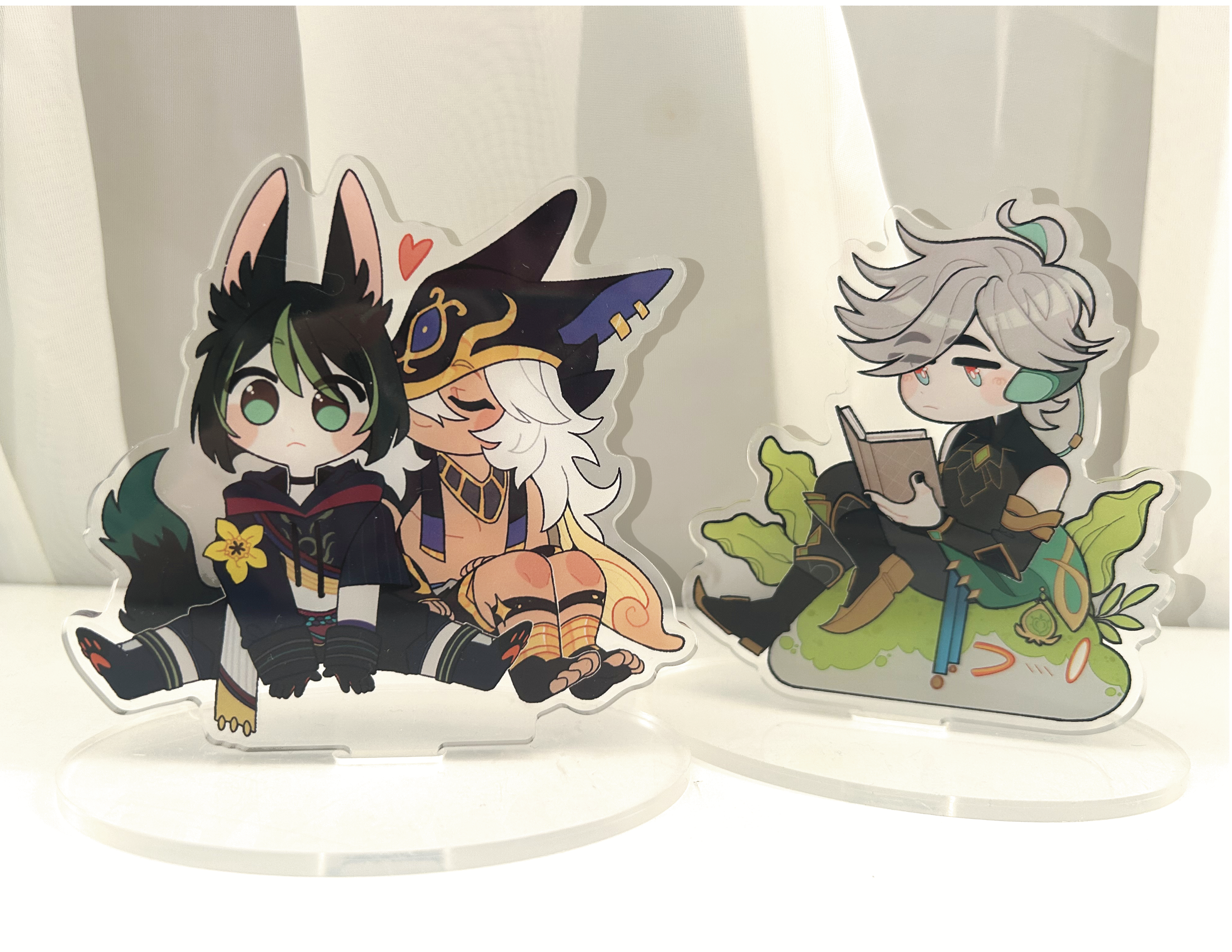 Acrylic standees , printed with an illustration of the ship "cynonari" as well as a standee of Alhaitham, placed on a light background.