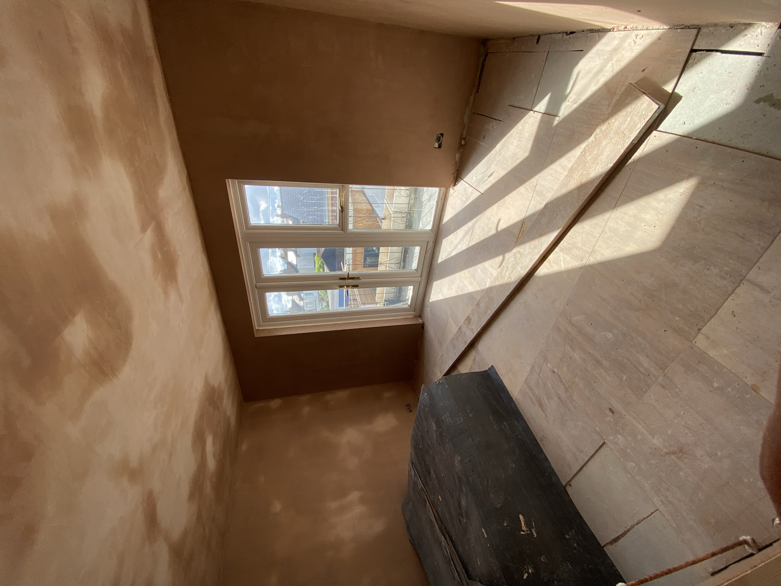 An unfinished room with a large window, with sunlight streaming in, and various tiles piled on the floor.