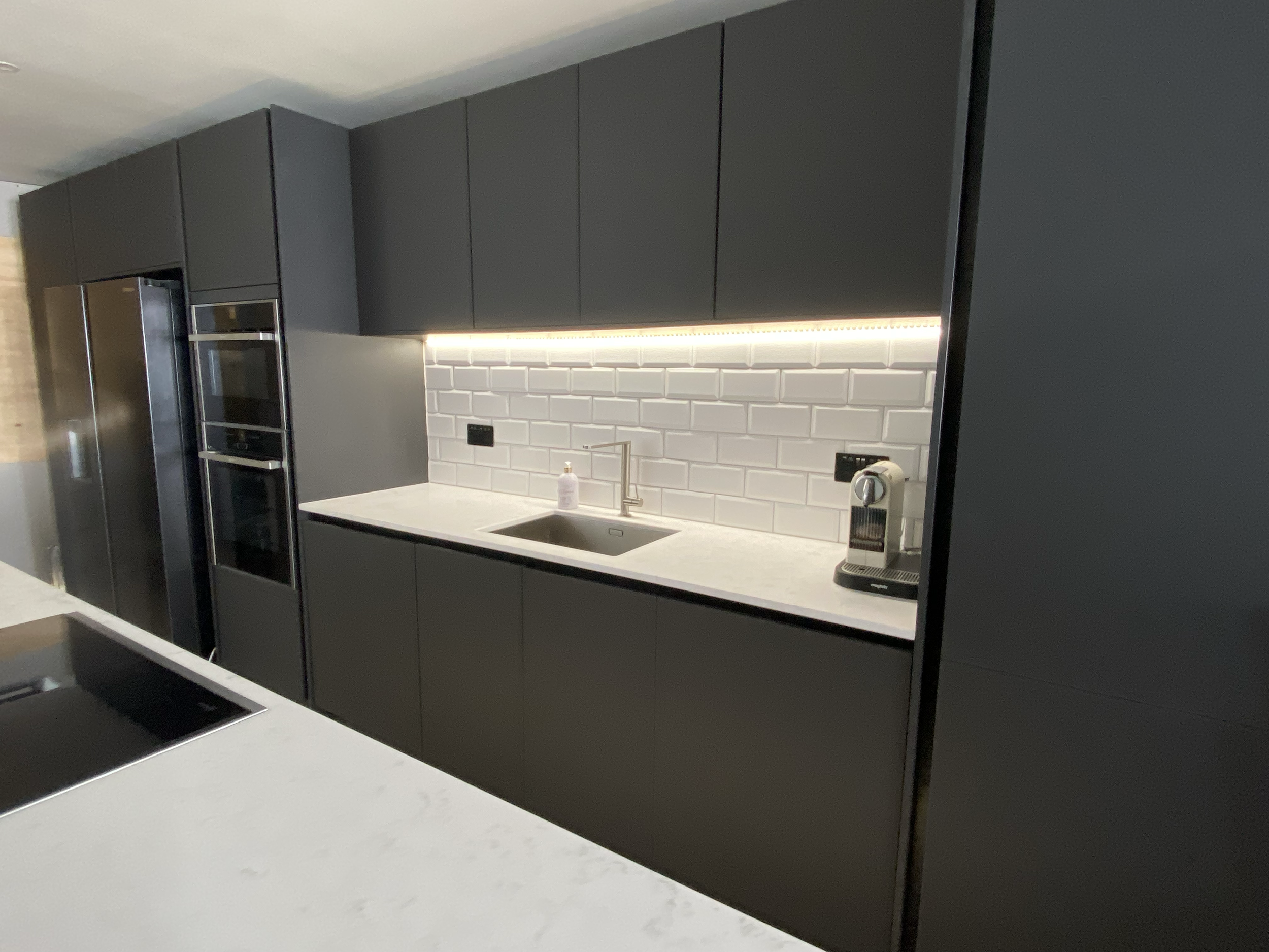 Modern kitchen with black cabinetry, white subway tile backsplash, and a white countertop featuring a sink and a small appliance.