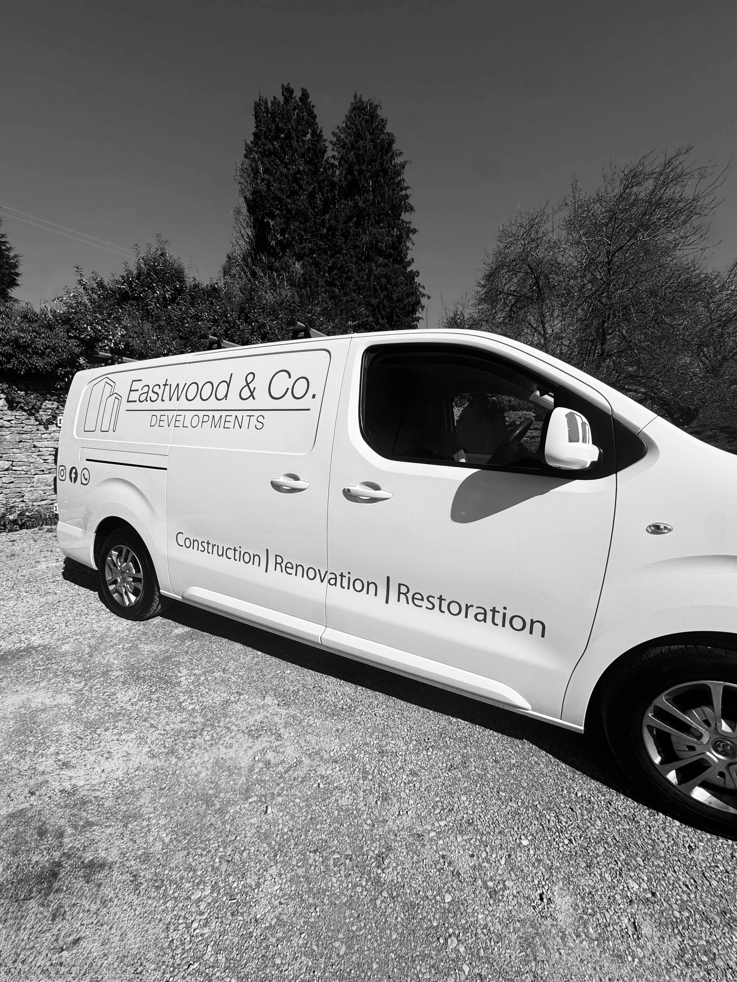 A white van with the logo and text 'Eastwood & Co. Developments' parked on a gravel surface with trees in the background.