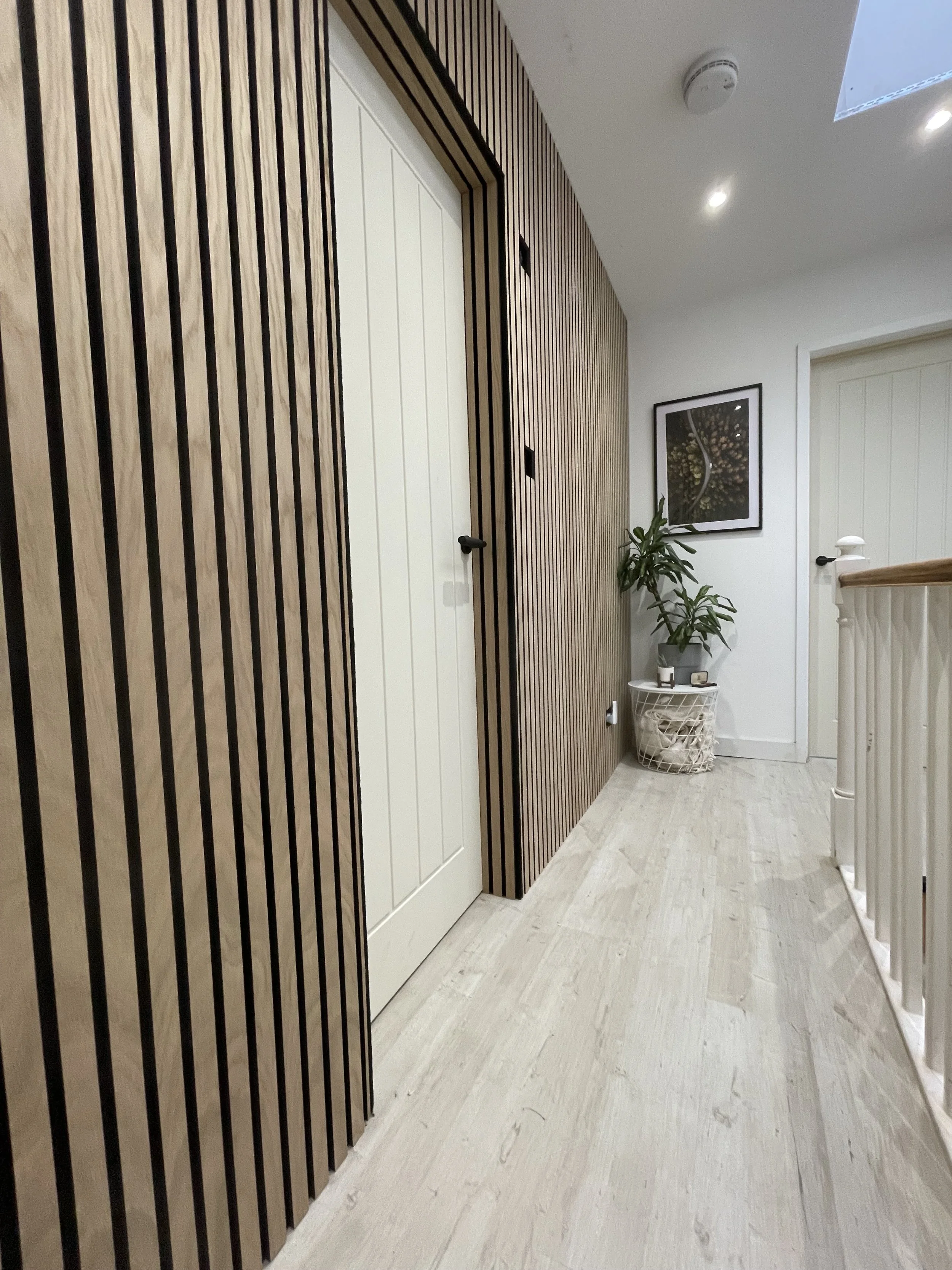 A hallway with a white door, wood paneling, framed artwork, a potted plant, and a basket