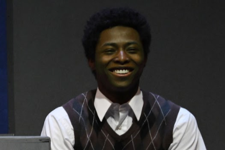 Smiling man with curly hair wearing a white shirt and a dark argyle vest.