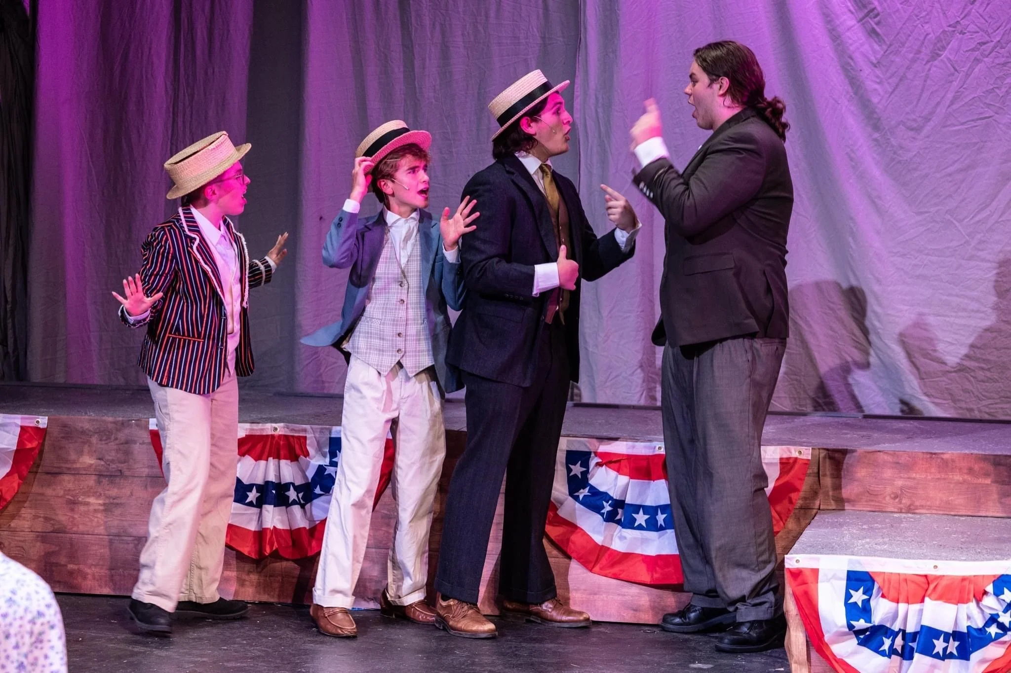 Actors performing on stage in a play, with three children and an adult, all dressed in costumes, and patriotic decorations in the background.