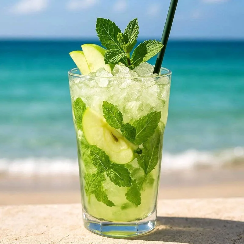 Verre de mojito contenant du citron, de la menthe, des glaçons, avec une paille noire, sur fond de plage et mer.