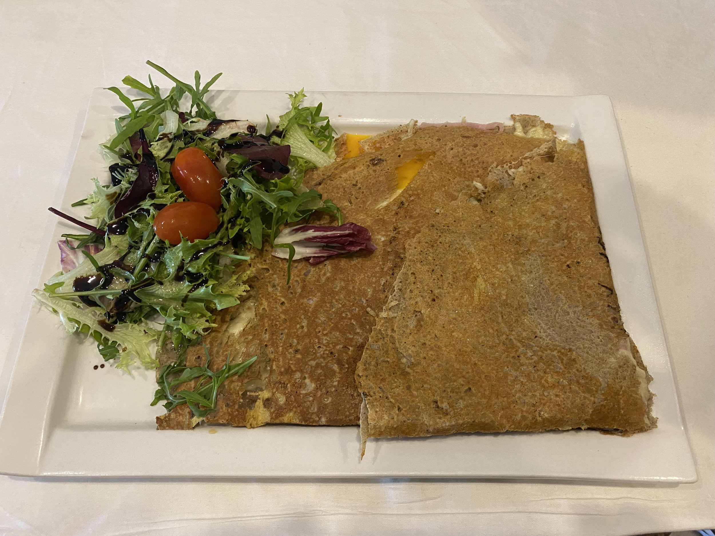 Une assiette avec une portion de salade verte accompagnée de tomates cerises et d'une part de galette ou de crêpe salée.