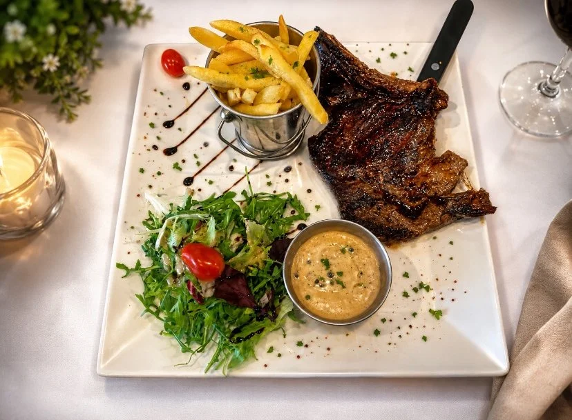 Plate de viande grillée avec des frites, une petite salade verte, une petite sauce, et un verre de vin rouge à côté.